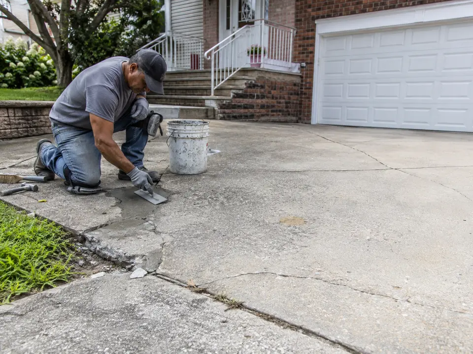 Worker repairing a damaged section of concrete near a residential garage entrance.