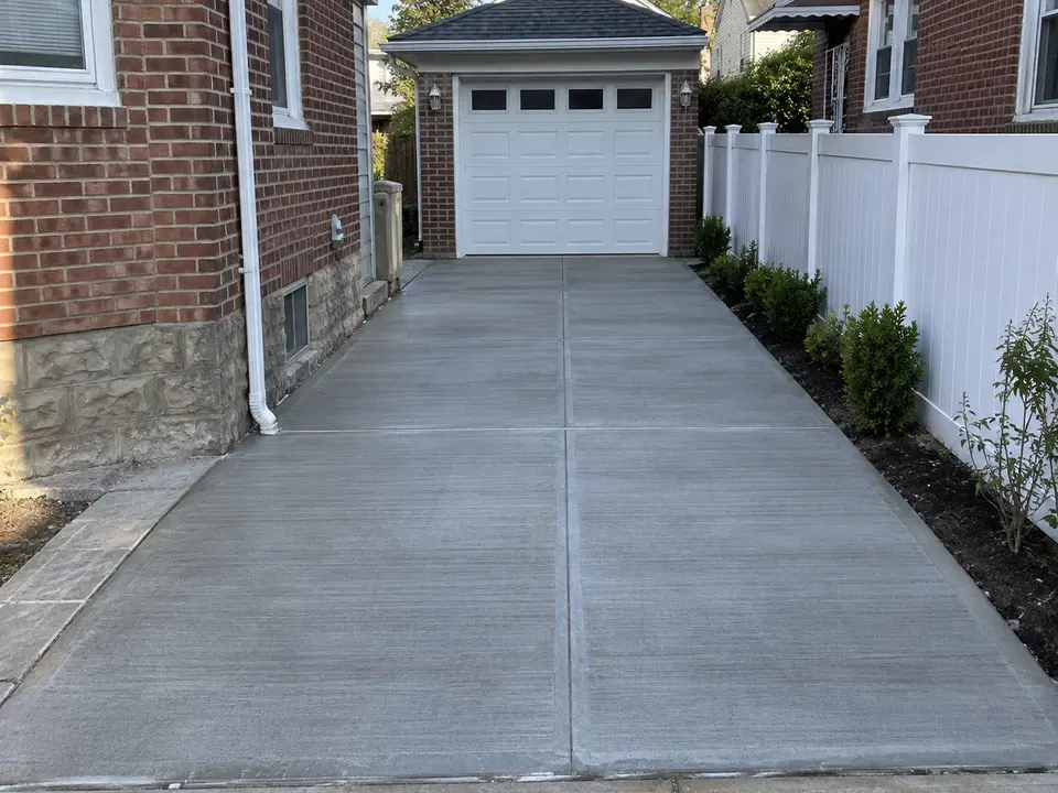 Newly finished concrete driveway with a textured surface and control joints leading to a residential garage.