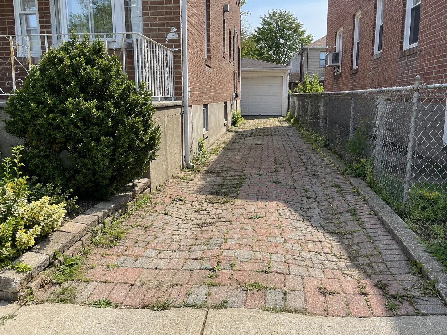Worn brick-paver driveway with uneven paving stones and deteriorated joints leading toward a residential garage.