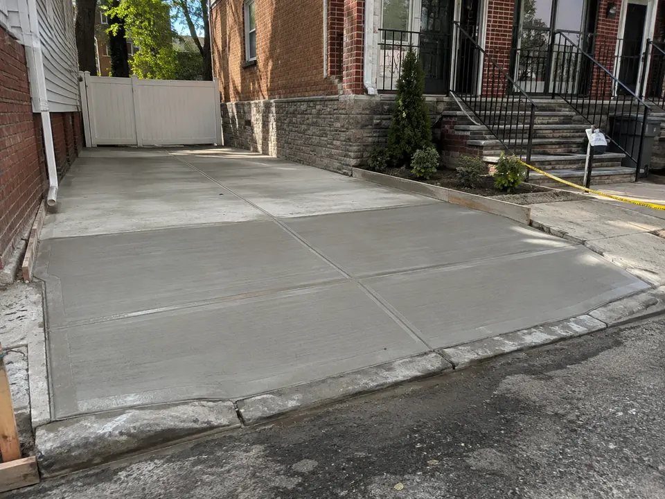 Freshly finished concrete at a residential driveway entrance beside a brick building.