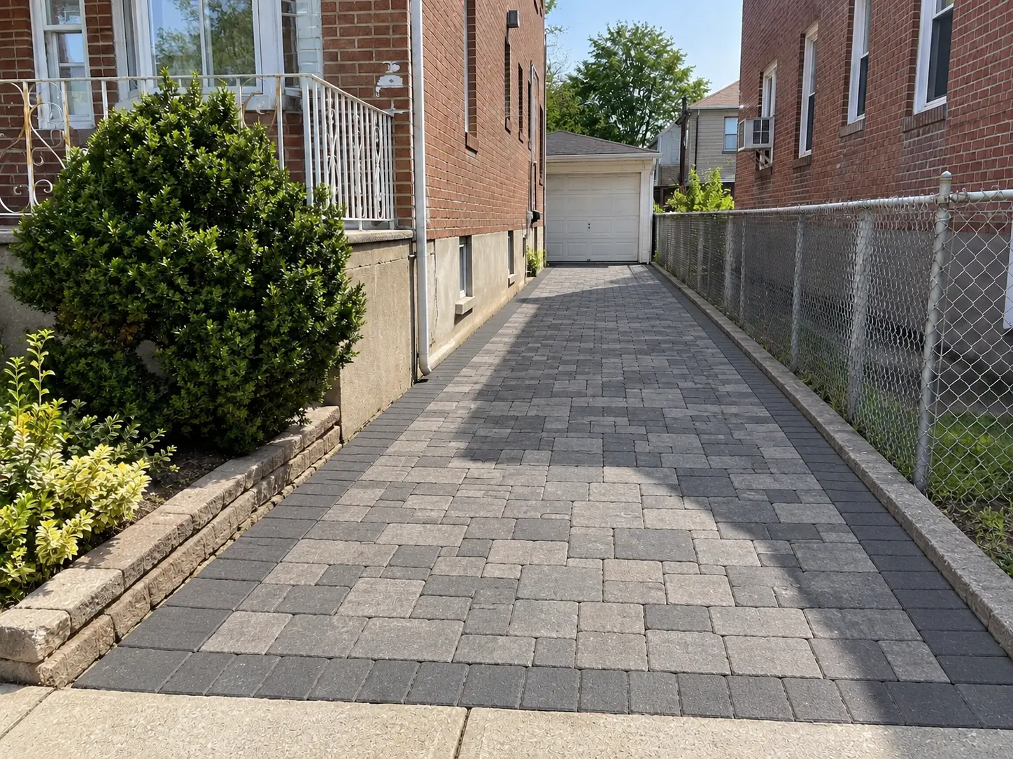 Gray interlocking concrete-paver driveway with a patterned surface leading toward a residential garage.
