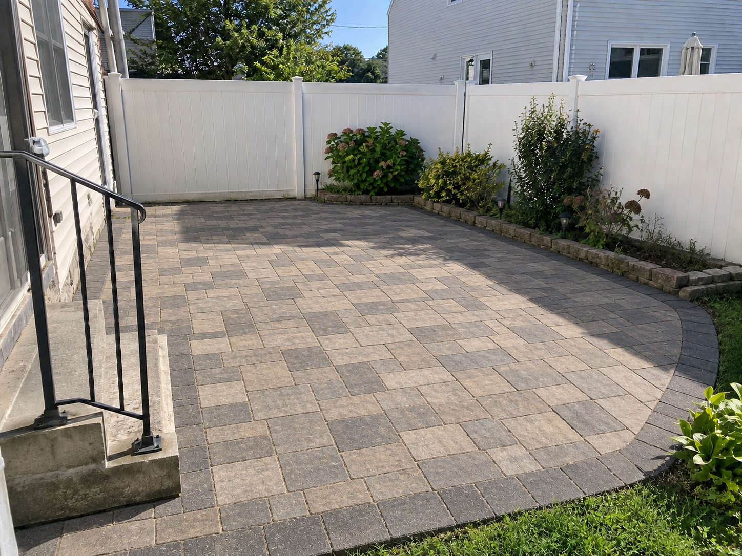 Finished patio with gray interlocking concrete pavers arranged in a patterned layout beside a white privacy fence.
