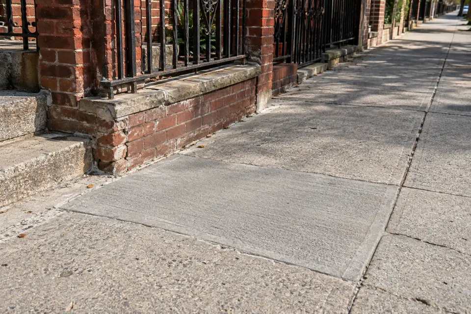 Repaired concrete sidewalk beside a brick residential property in New York City