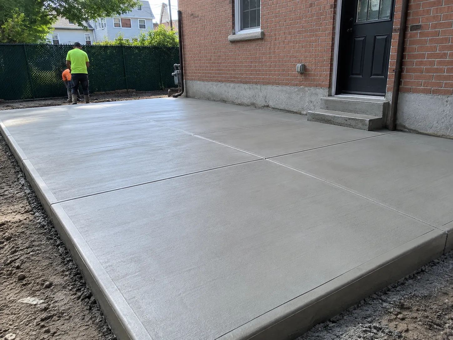 Newly installed concrete slab with a smooth broom-finished surface and control joints outside a residential property in NYC.