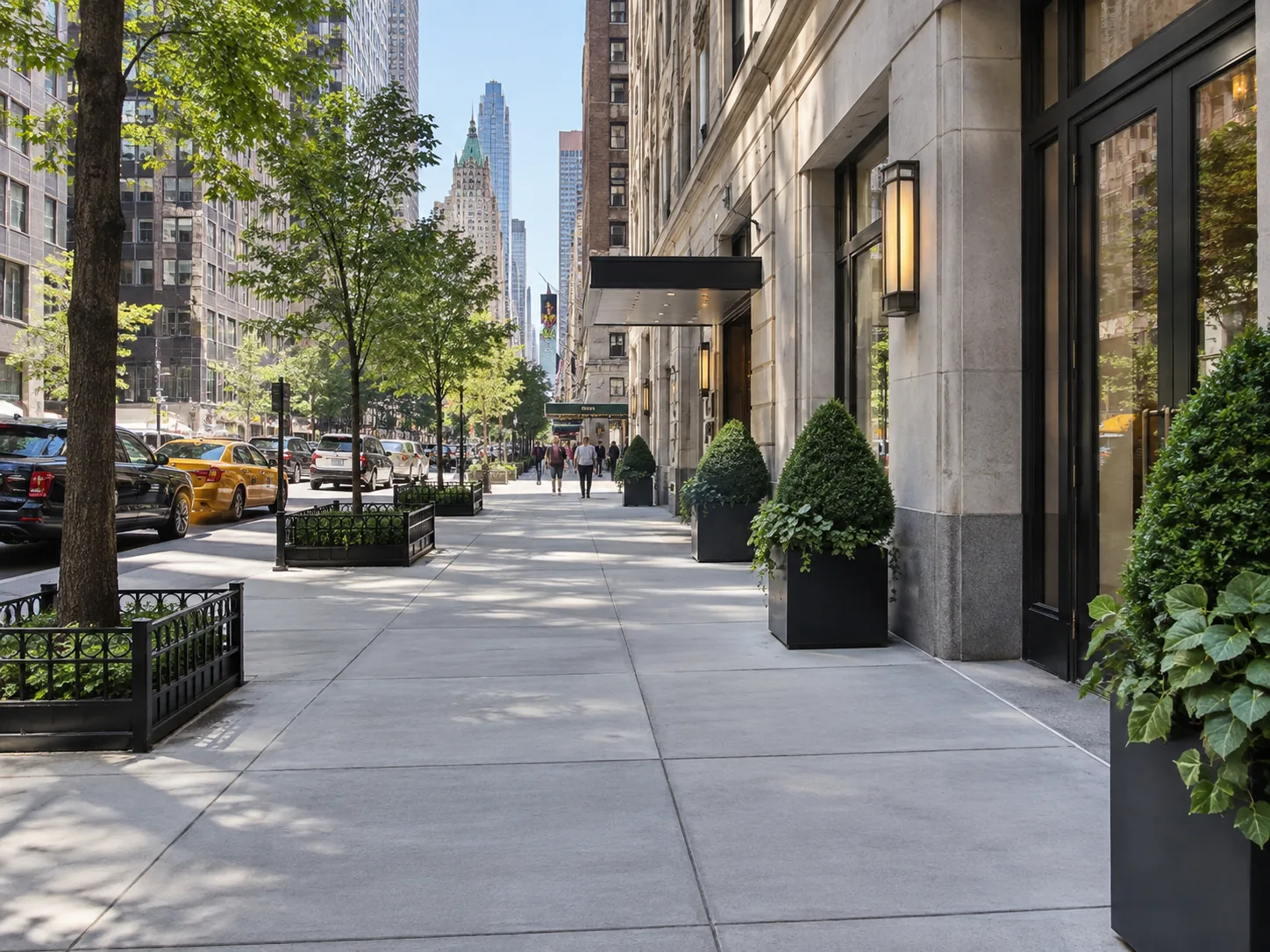 Wide concrete sidewalk outside a Manhattan commercial building with high-rise architecture, storefront entrances and street trees.
