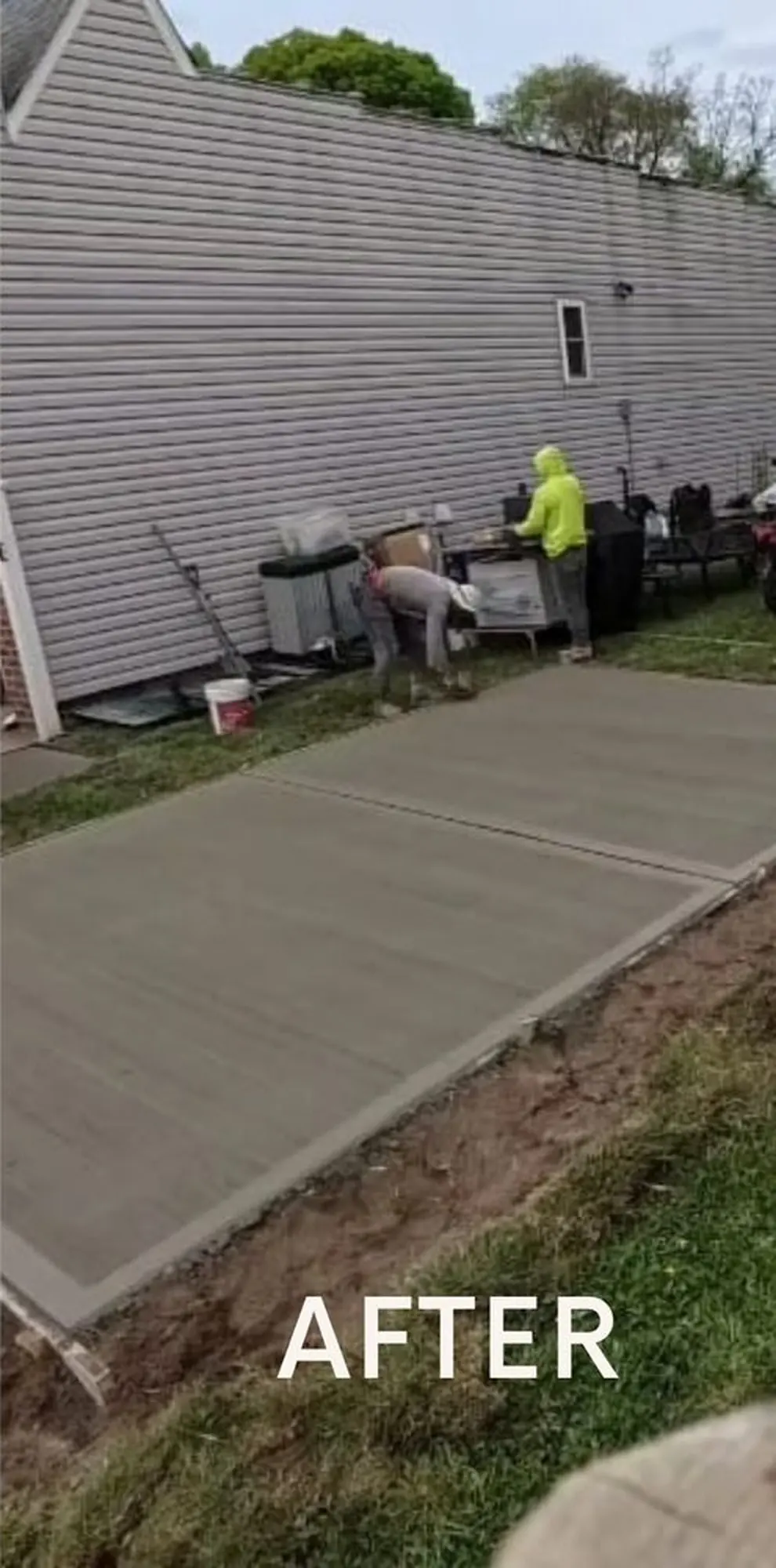Freshly finished concrete slab beside a residential building, with workers and construction equipment nearby.