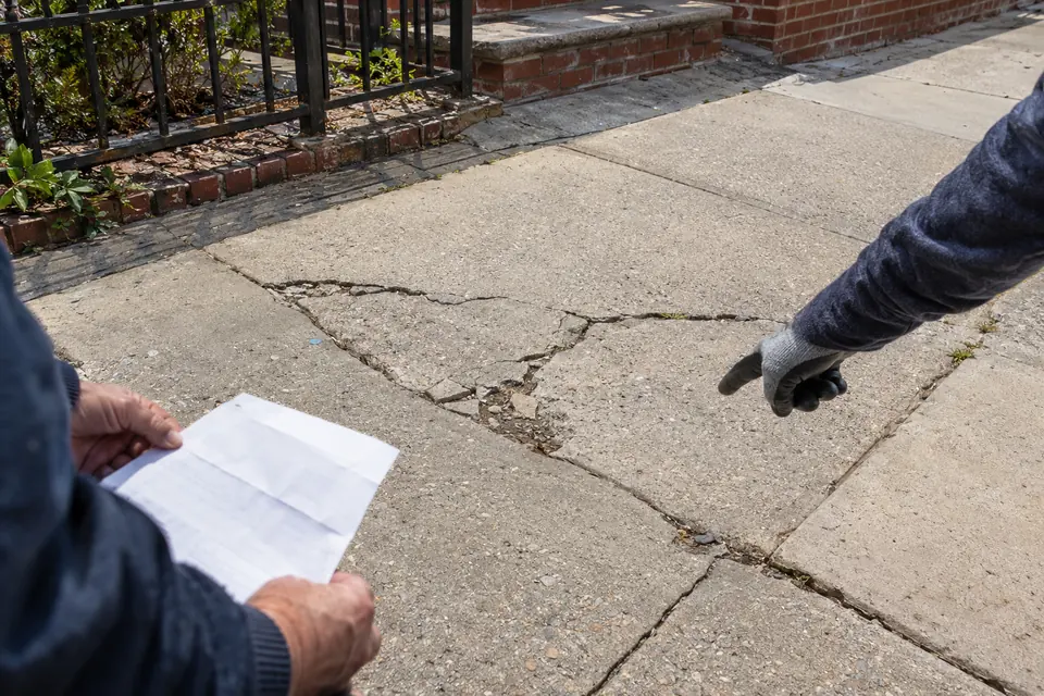 Contractor reviewing an NYC DOT sidewalk violation notice beside cracked concrete sidewalk