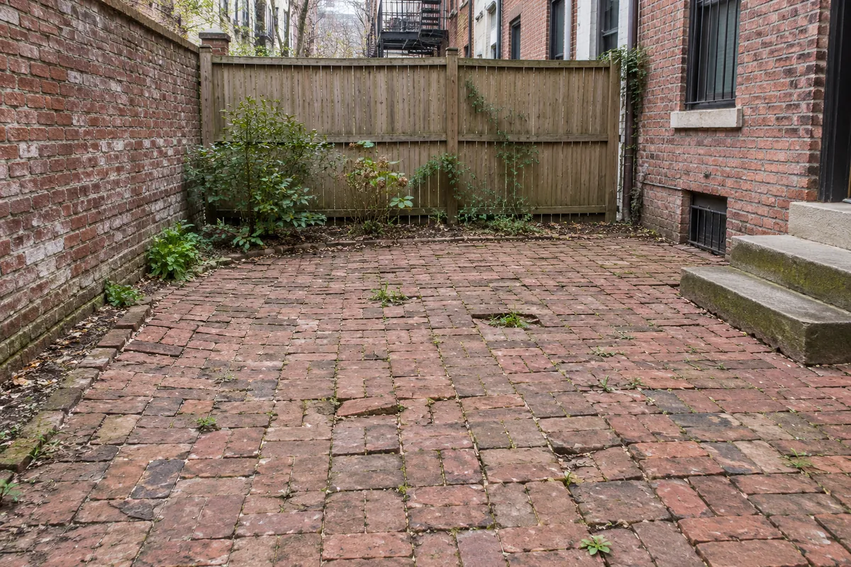 Aging red brick backyard patio with uneven pavers and weeds between joints.