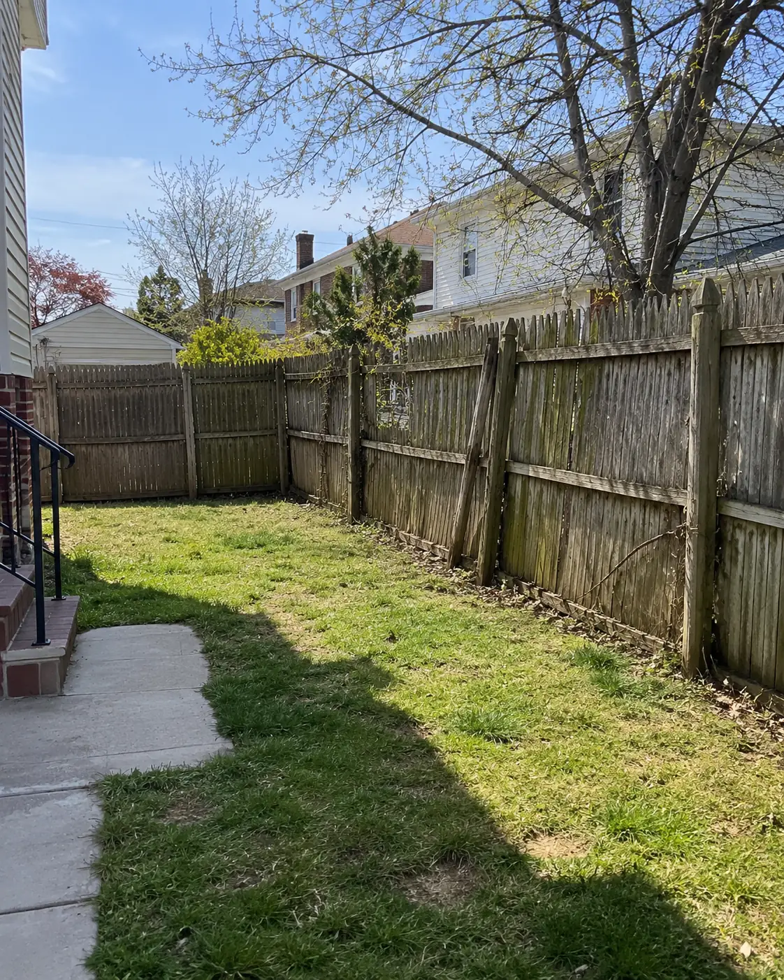Weathered and leaning wood privacy fence surrounding a residential backyard before replacement.